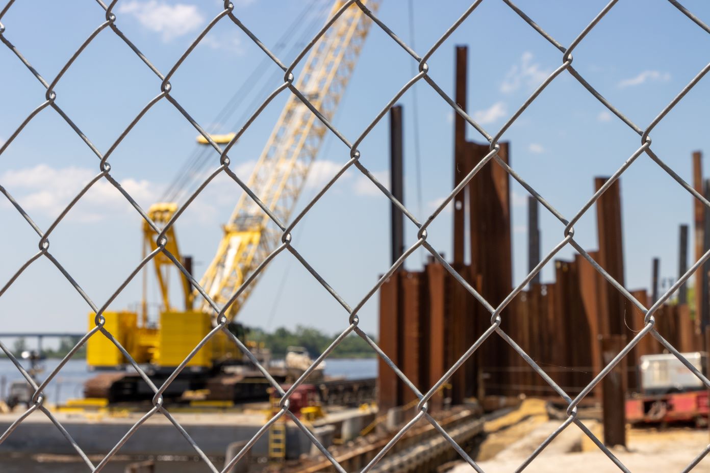 A crane works in a construction site, seen through a chain link fence