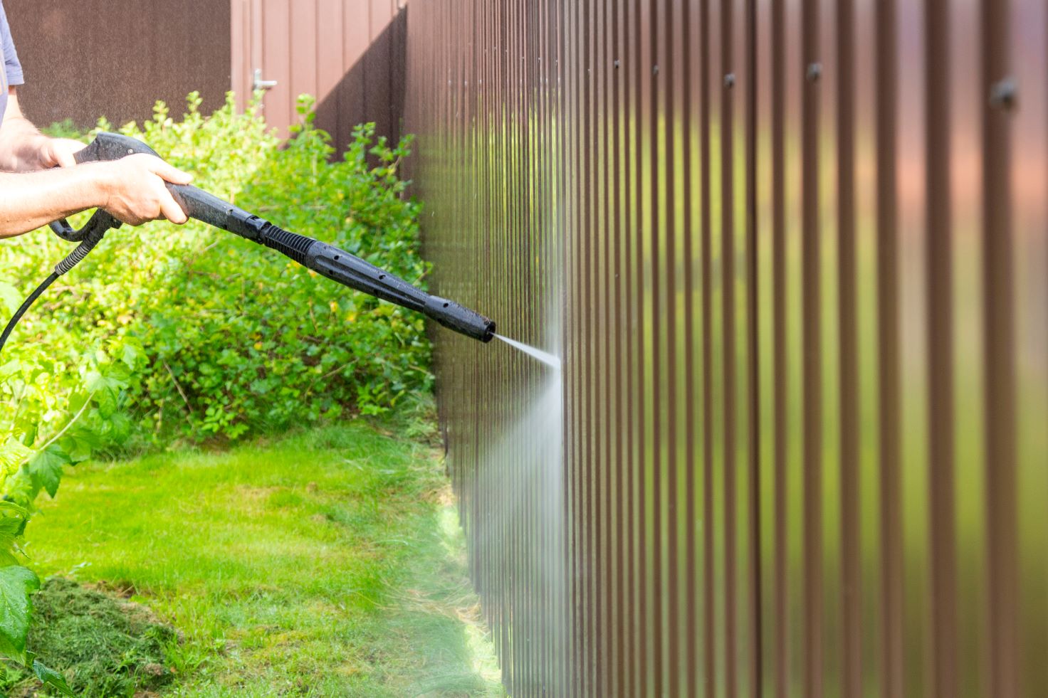 A powerwasher sprays a wooden fence to clean it.