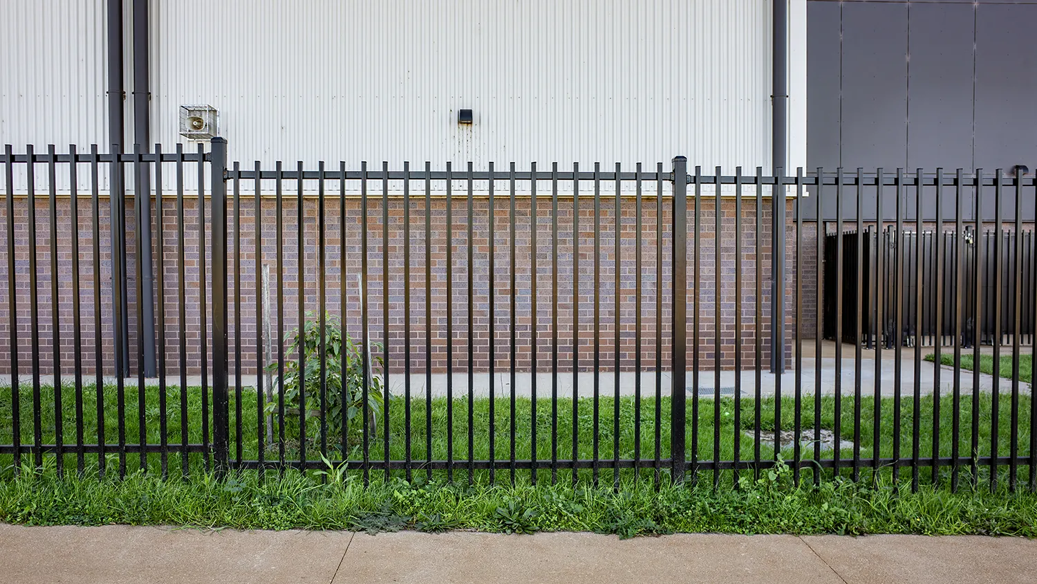 A black metal security fence installed along the exterior of a modern commercial or industrial building.